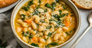 White bean soup in a bowl with spinach, carrots and parmesan cheese.