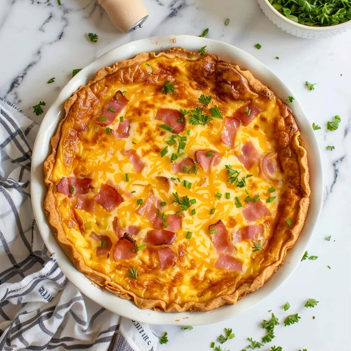 Whole ham and cheese quiche in a round pie dish on top of white marble table.