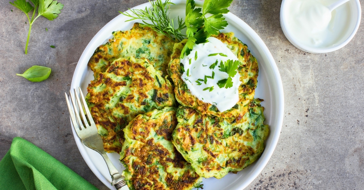 Zucchini fritters on a white plate garnished with dill and yogurt sauce.