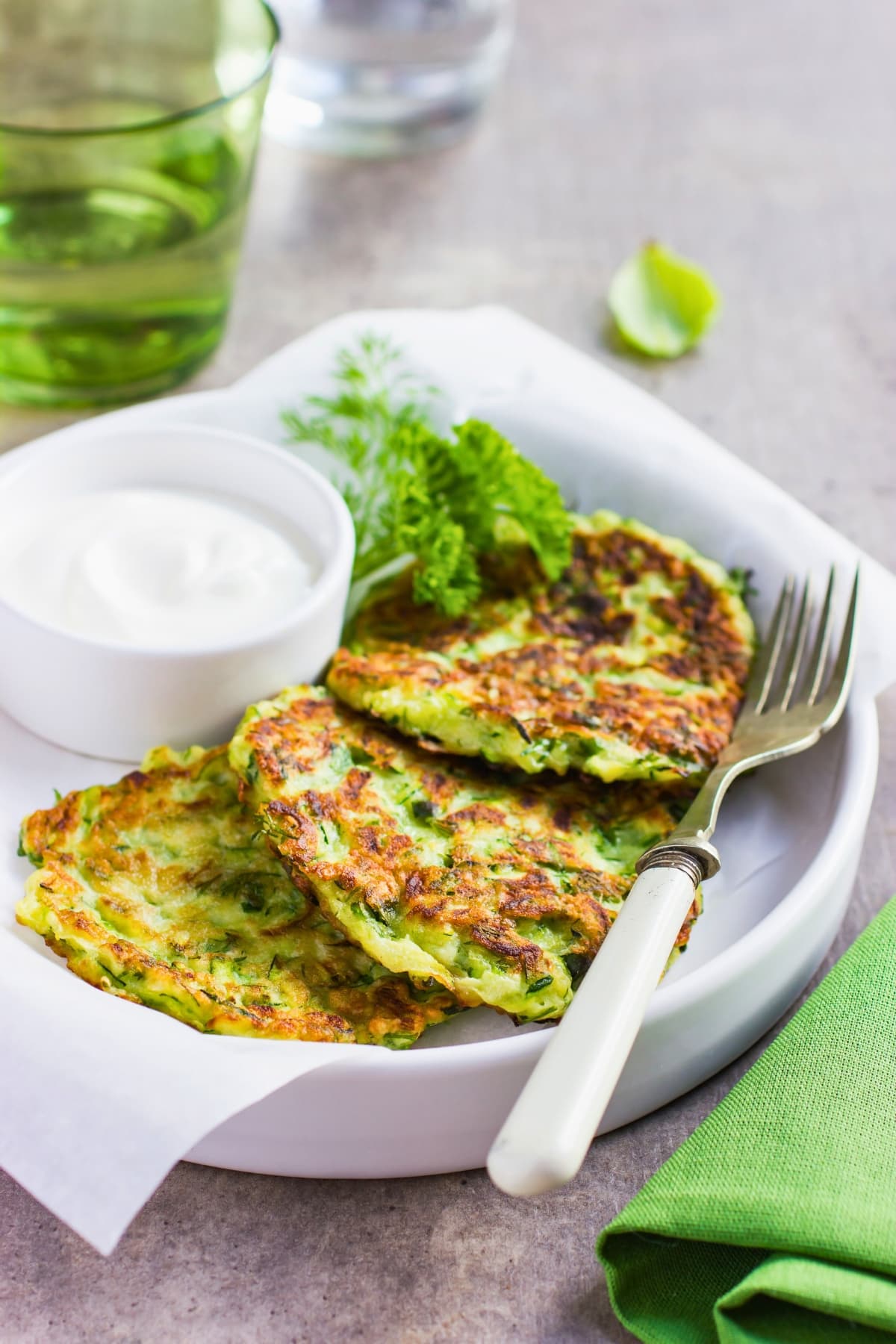 Zucchini fritters on a plate served with sour cream garnished with fresh dills.