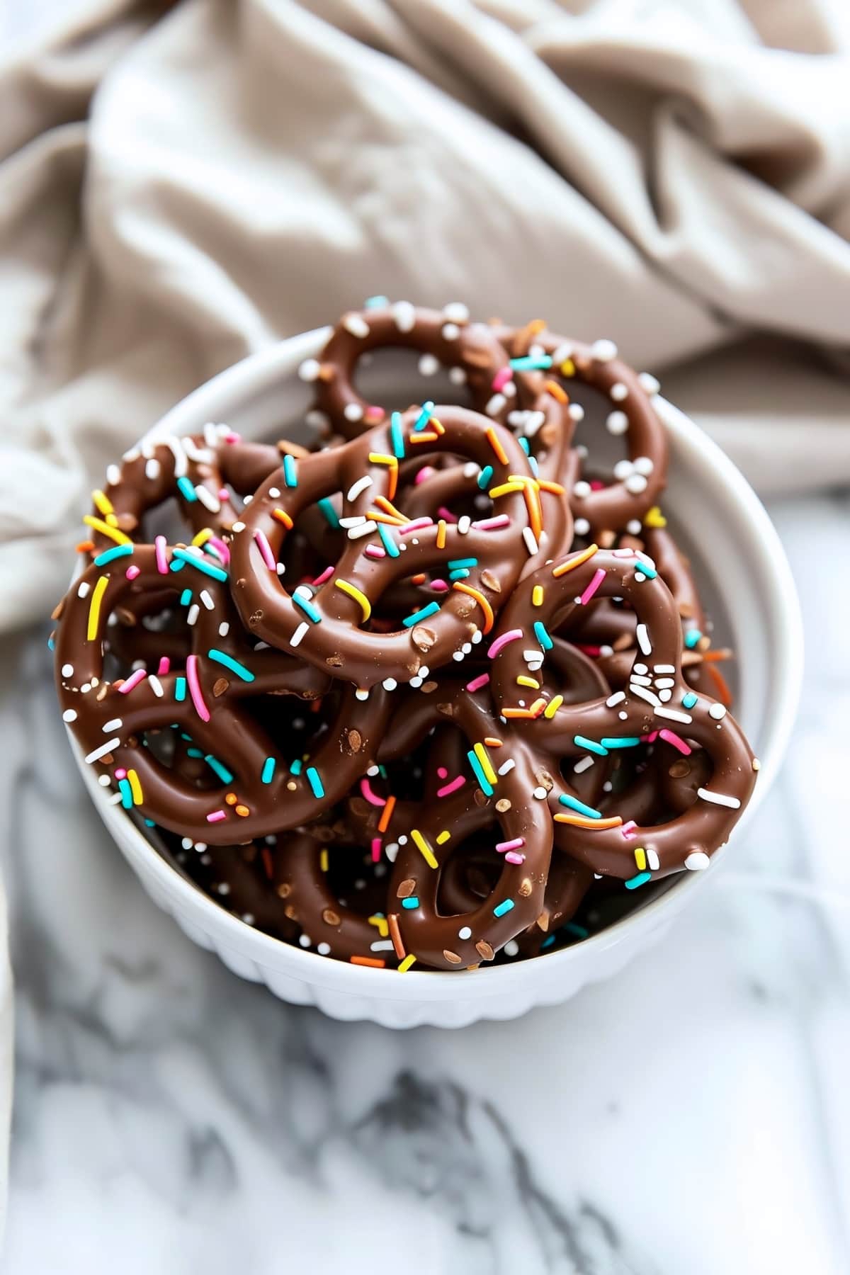 Sweet homemade chocolate covered pretzels with sprinkles in a white bowl