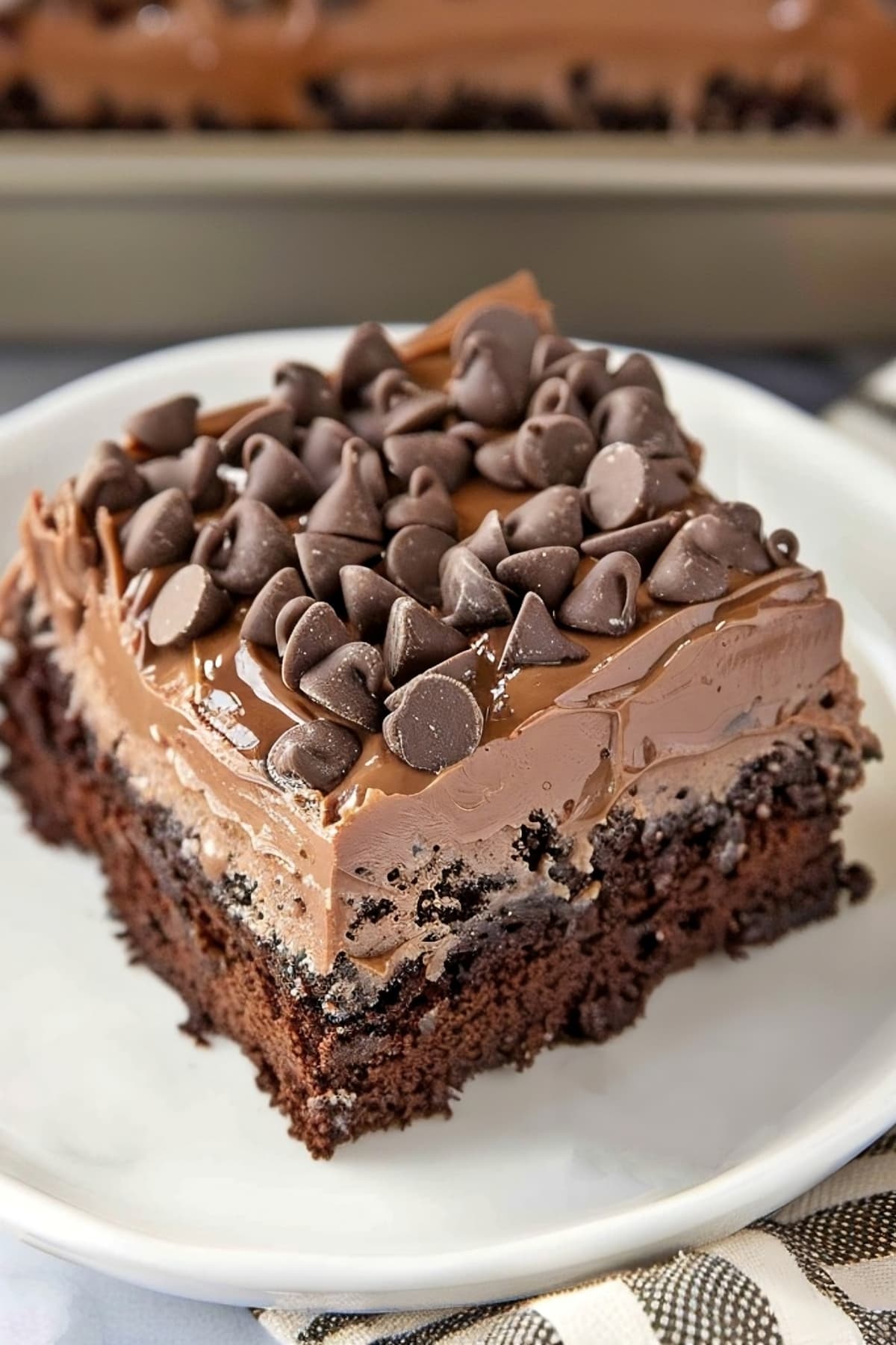 A piece of chocolate poke cake topped with chocolate chips on a white plate