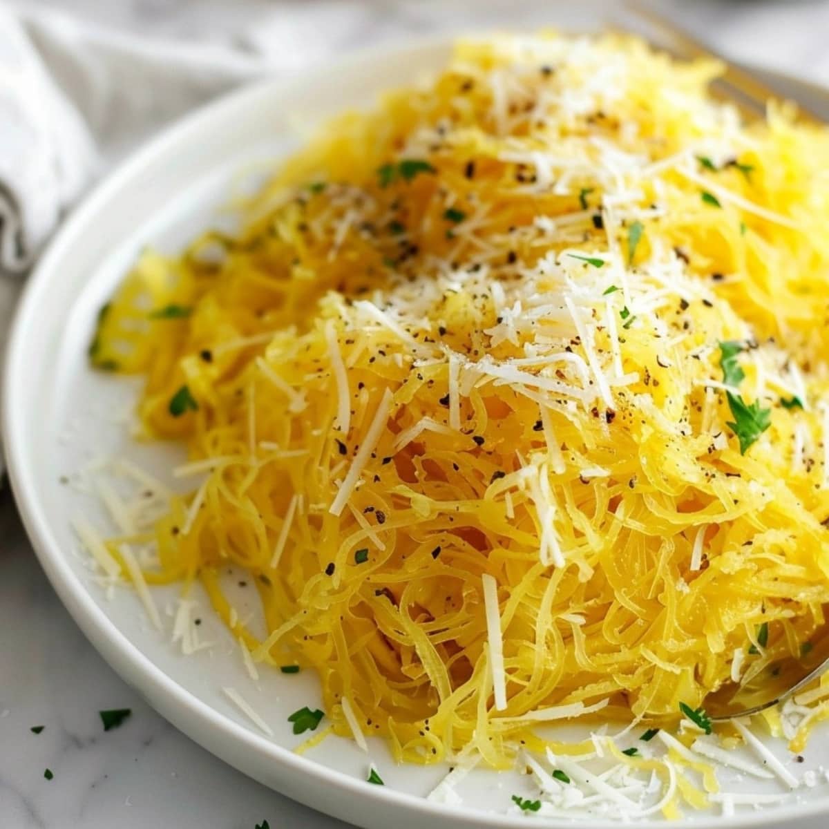 Air fried spaghetti squash served on a white plate garnished with grated parmesan cheese.