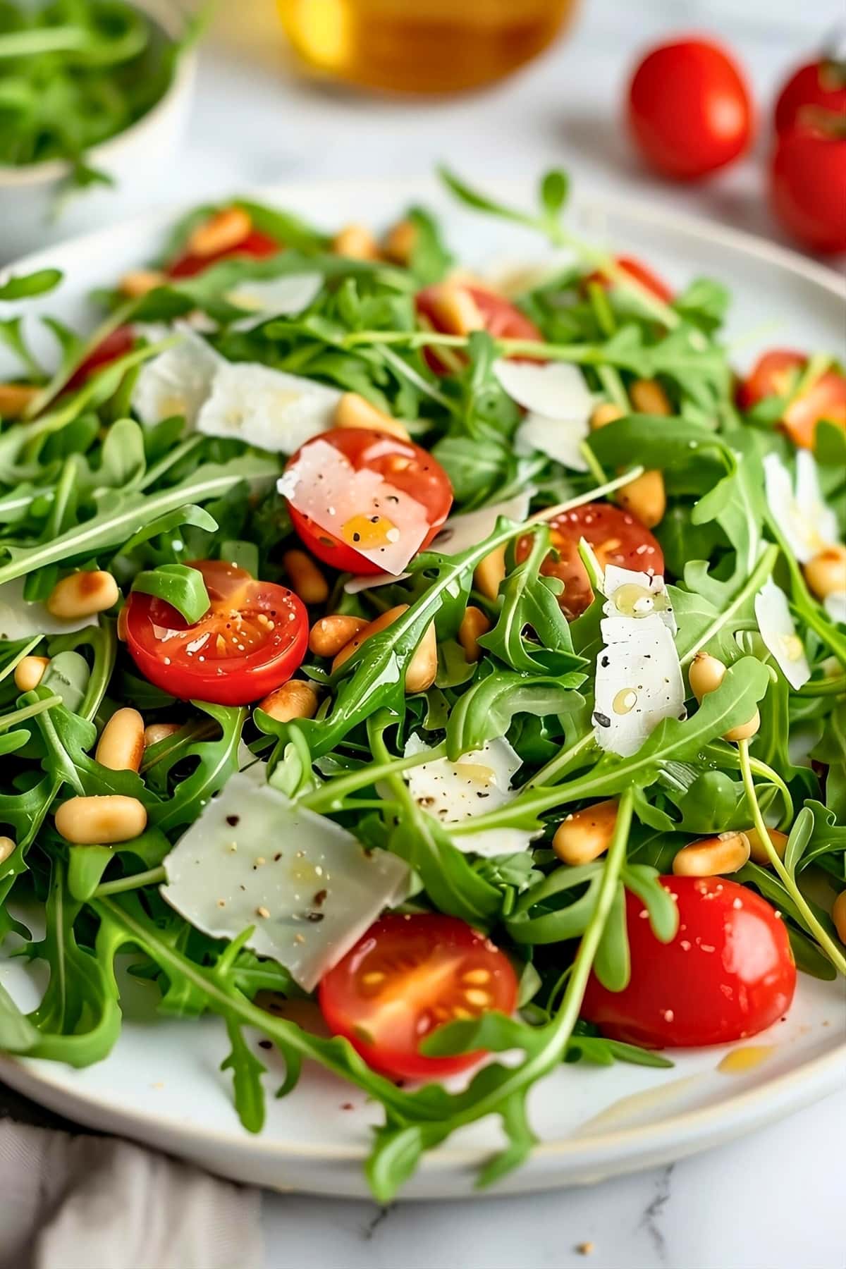 Arugula salad served on a white plate with cherry tomatoes, nuts and fresh arugula drizzled with lemon dressing.