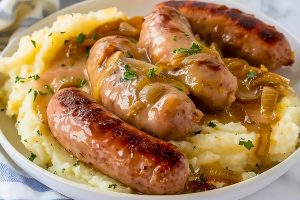 Mashed potatoes in a plate topped with sausage and onion gravy.