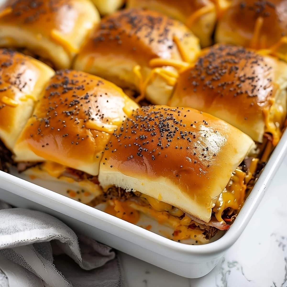 Cheese and beef sliders with poppy seeds on top on a baking dish.