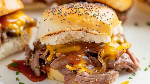 Beef and cheddar cheese sliders with poppy seeds on top served on a white plate.