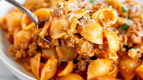 Spoonful shells in creamy and beefy tomato sauce from a white plate.