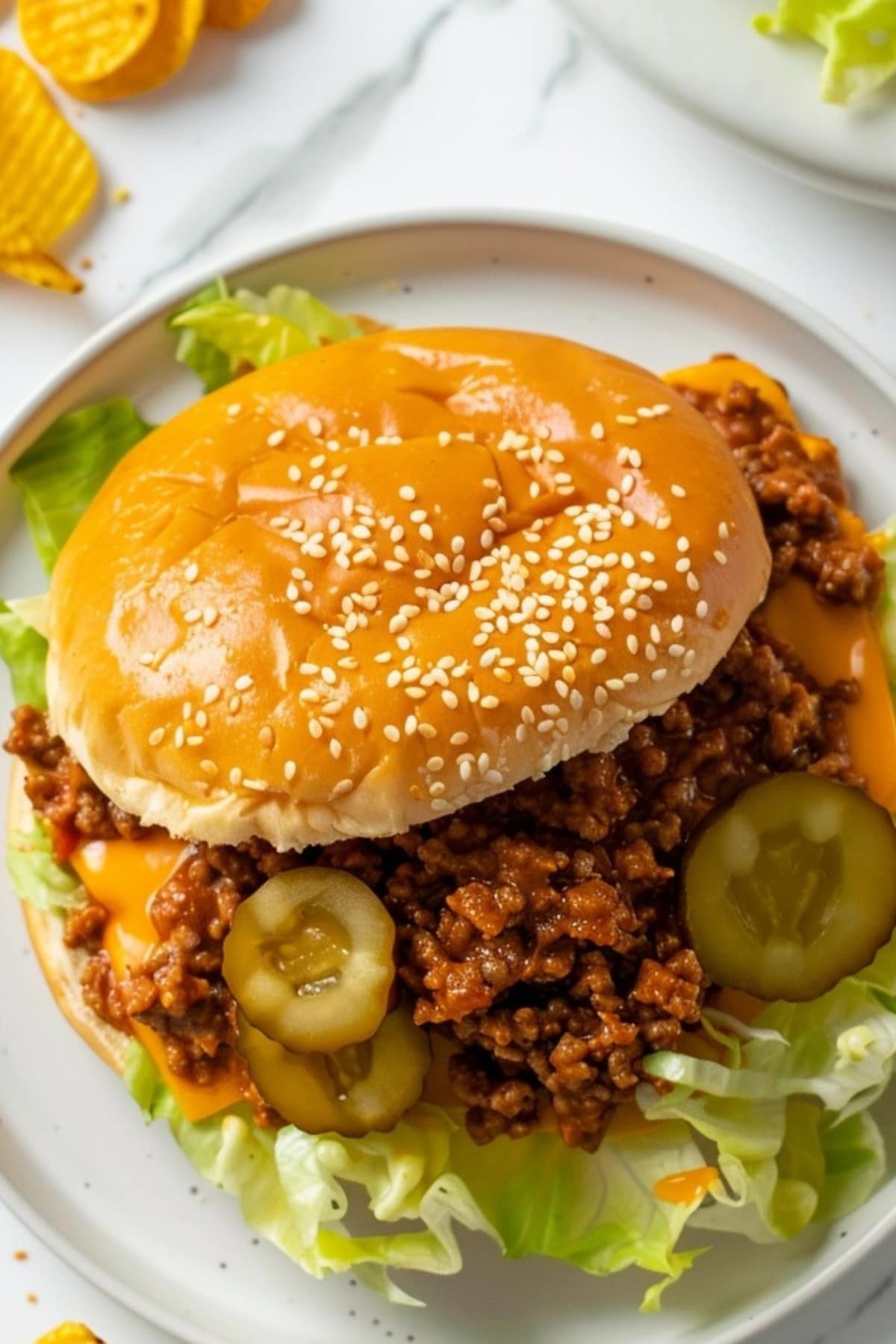Angled view of meaty and cheesy Big Mac Sloppy Joe in a plate with lettuce, melted cheese and dill pickles.