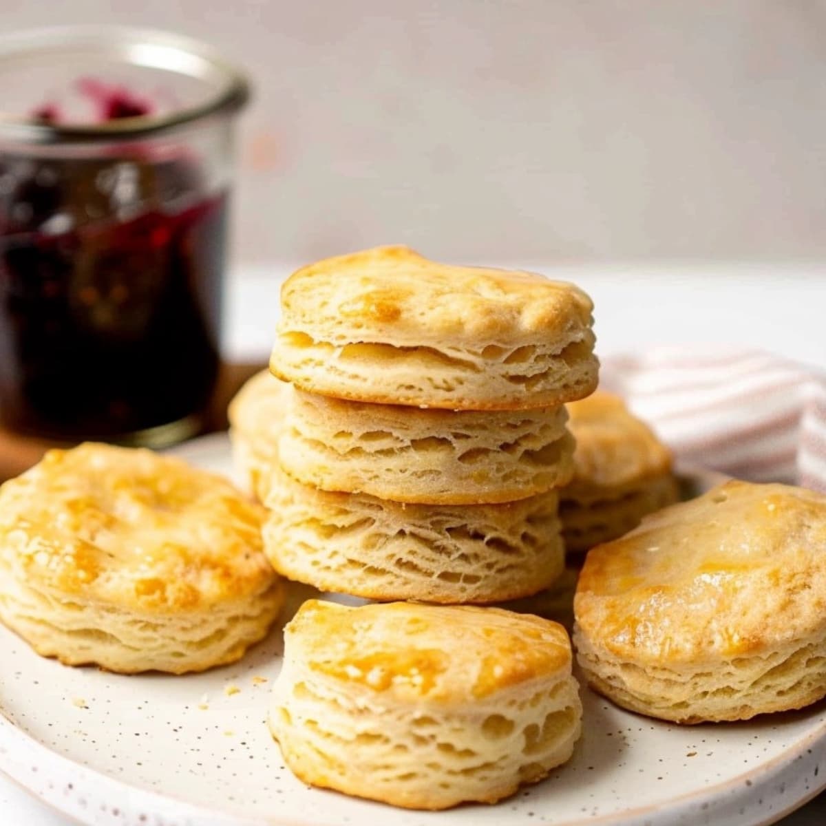 Biscuits in plate with jar of blueberry jam in the background.