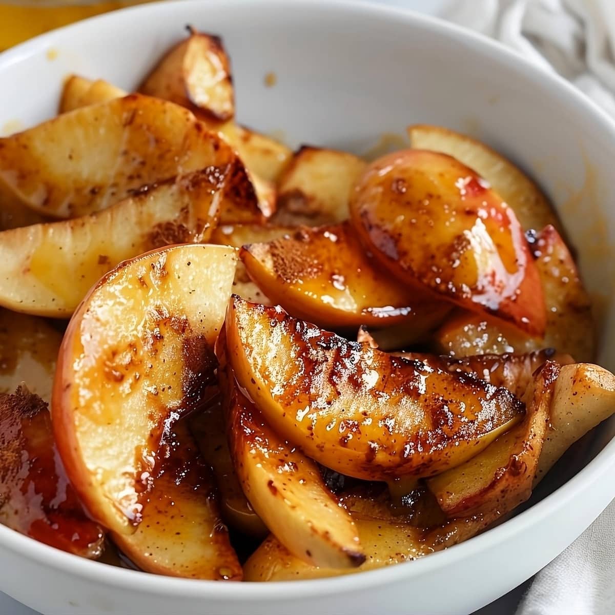 Baked apple slices with cinnamon, sugar and butter served on a white bowl.