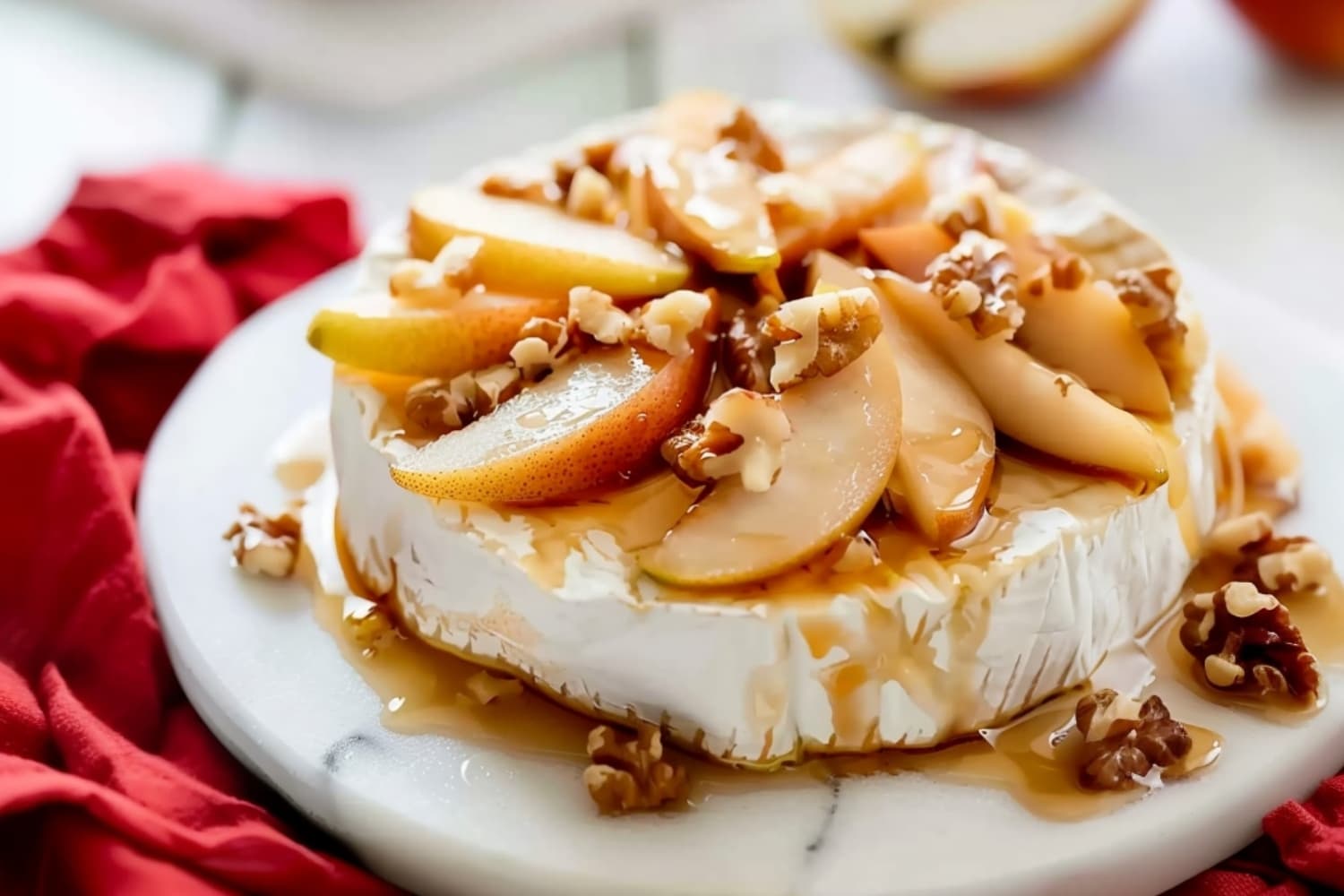 Caramelized pear and baked brie with chopped walnuts on a white marble table