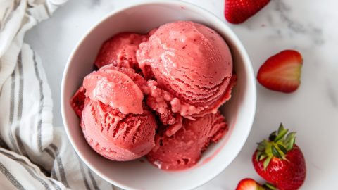 Strawberry sorbet in a bowl surrounded with fresh fruits on a white marble table