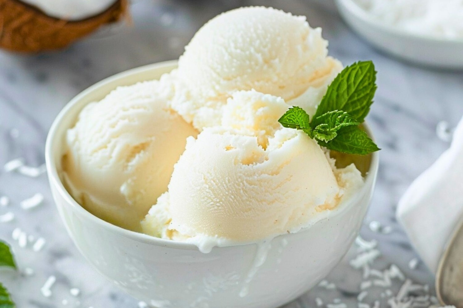 White bowl with scoops of coconut sorbet garnished with mint leaves.