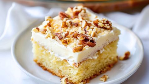 A slice of cake with chopped pecans and cream cheese frosting sitting in a white plate