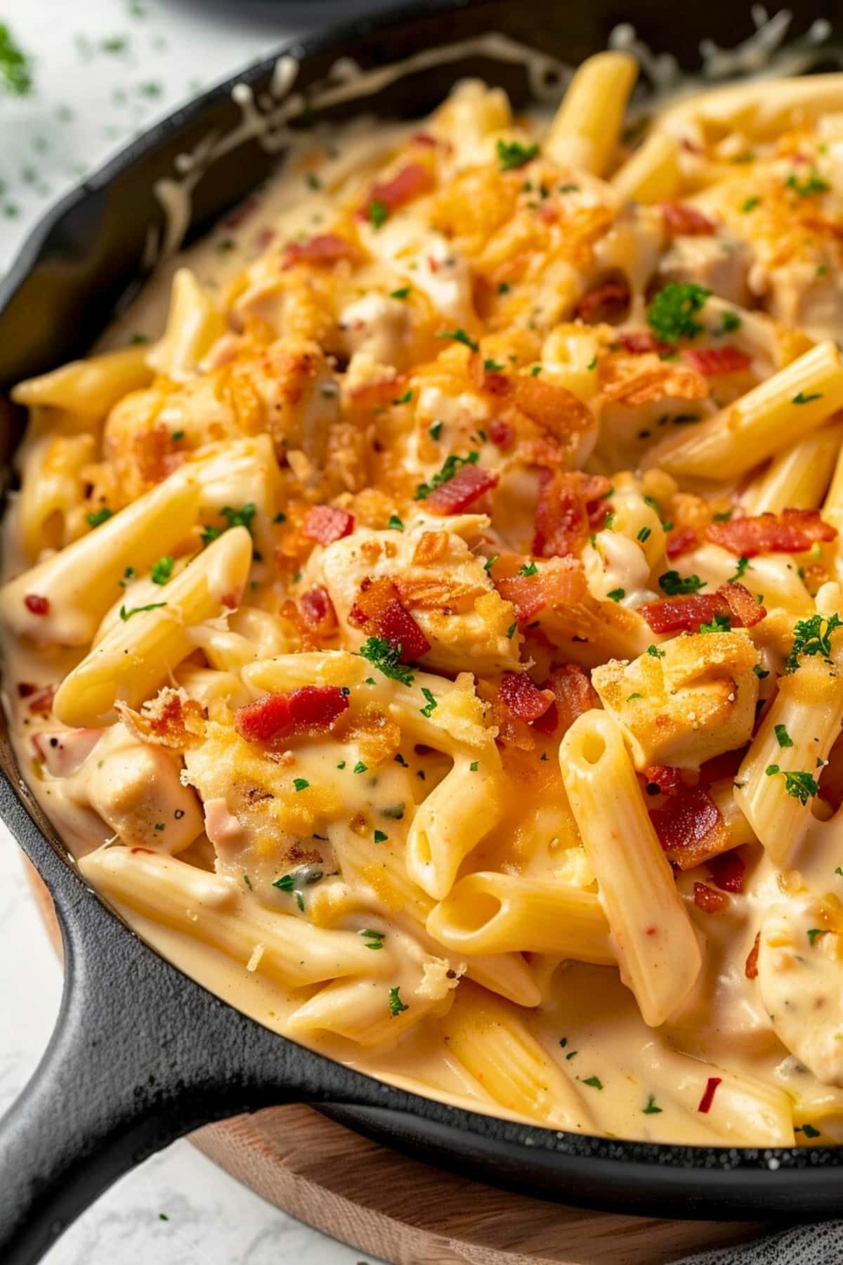 Penne pasta in cheesy and creamy sauce with chicken breast and fried bacon in a cast iron skillet.