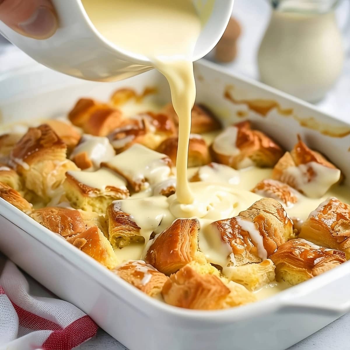 Creamy milk mixture poured in a baking dish with cubes of croissant