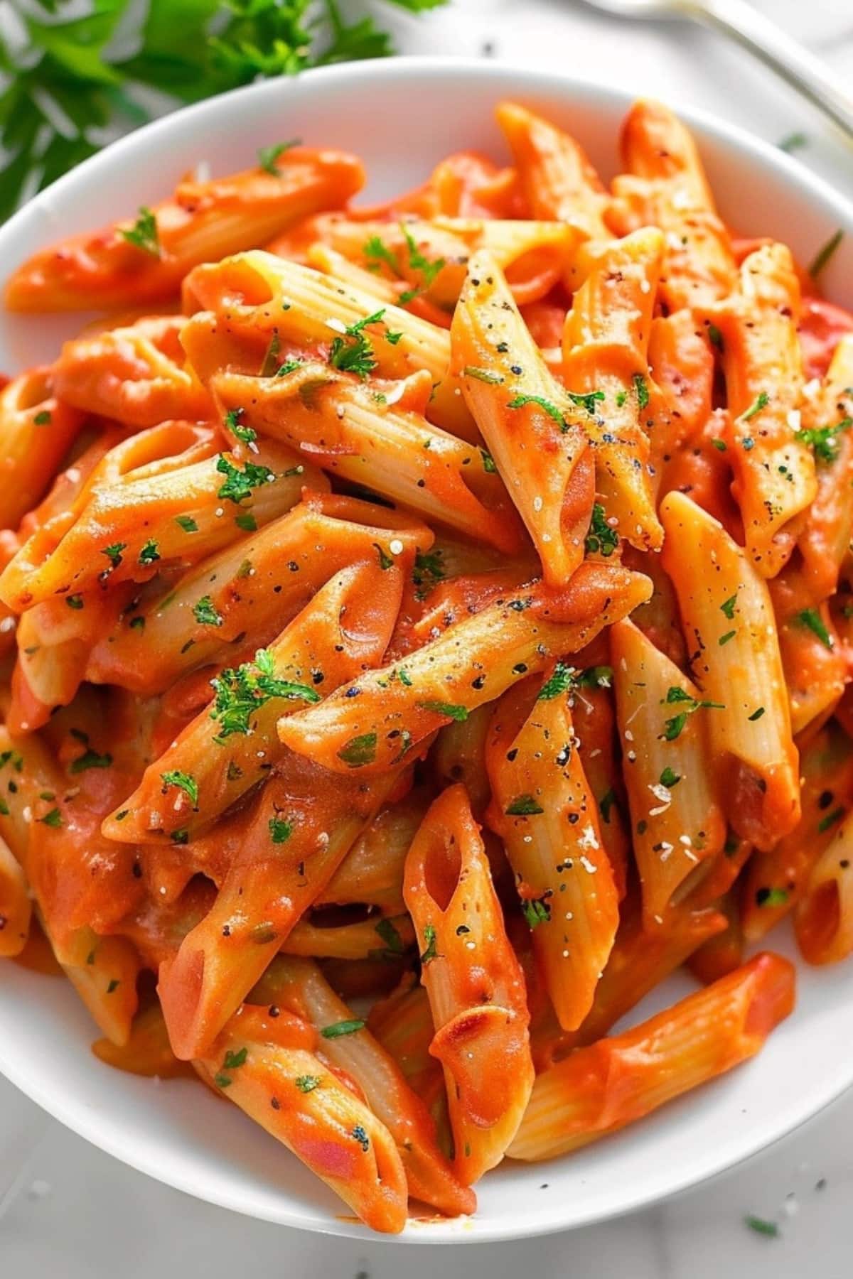 Penne pasta with cream vodka tomato sauce served on a white plate garnished with chopped parsley leaves.