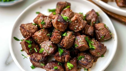 Homemade garlic butter steak bites in a white plate on a white marble table