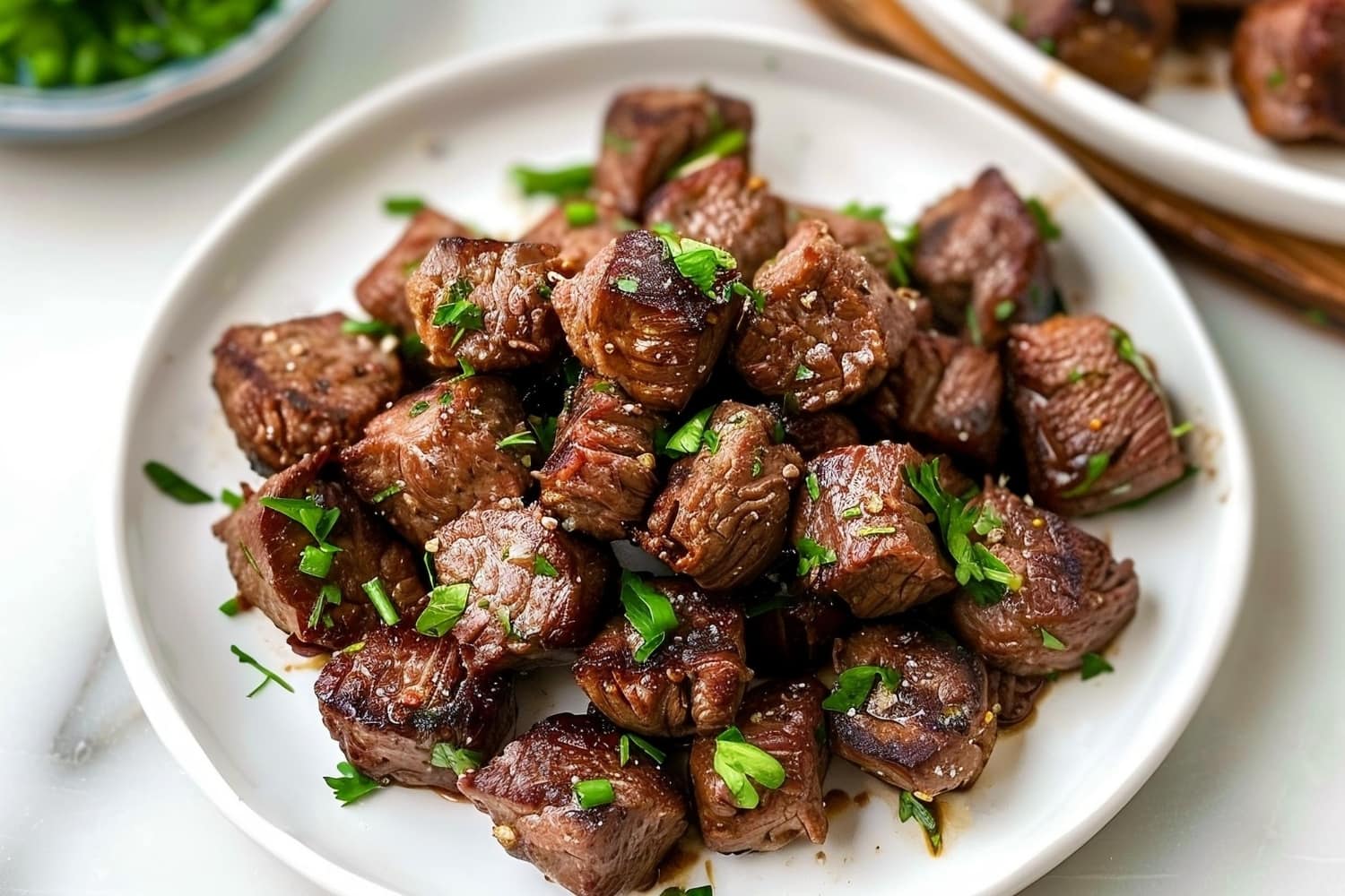 Homemade garlic butter steak bites in a white plate on a white marble table