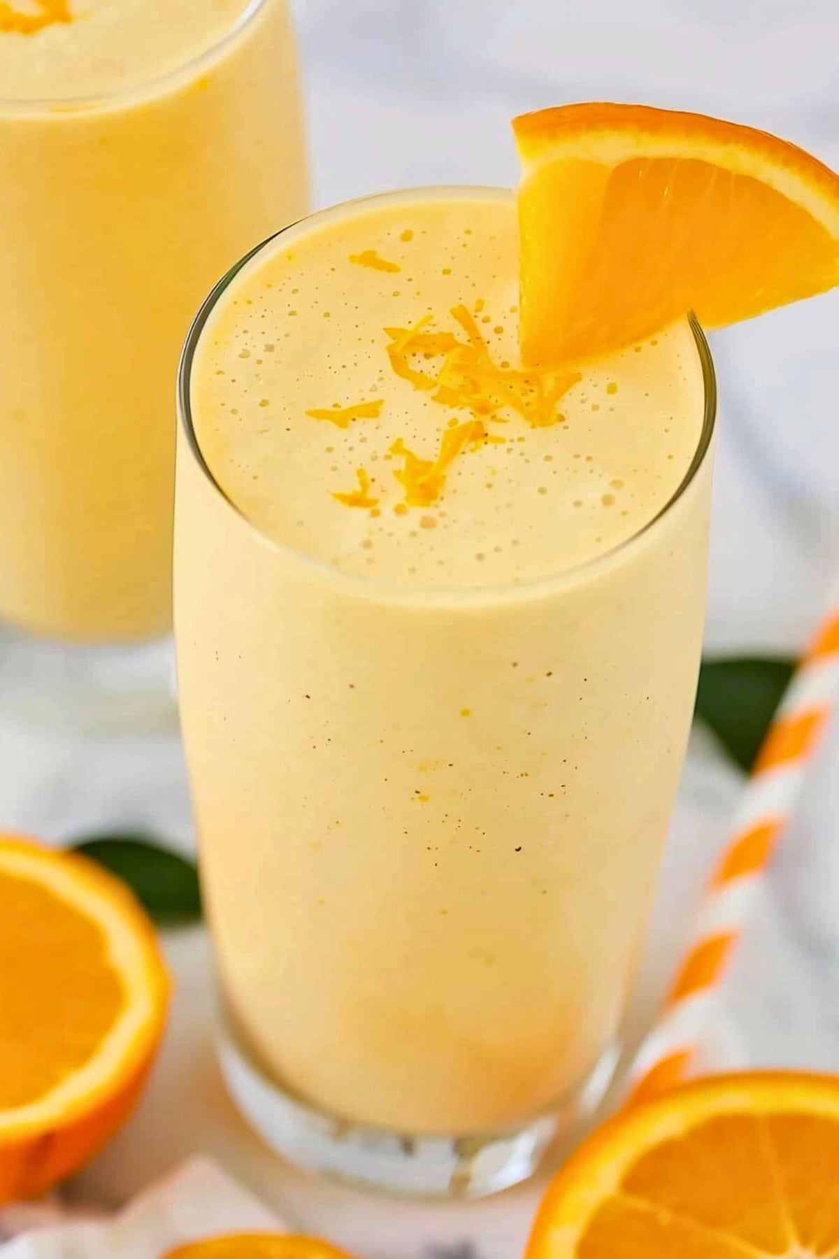 Orange smoothie in a tall glass garnished with orange slice.