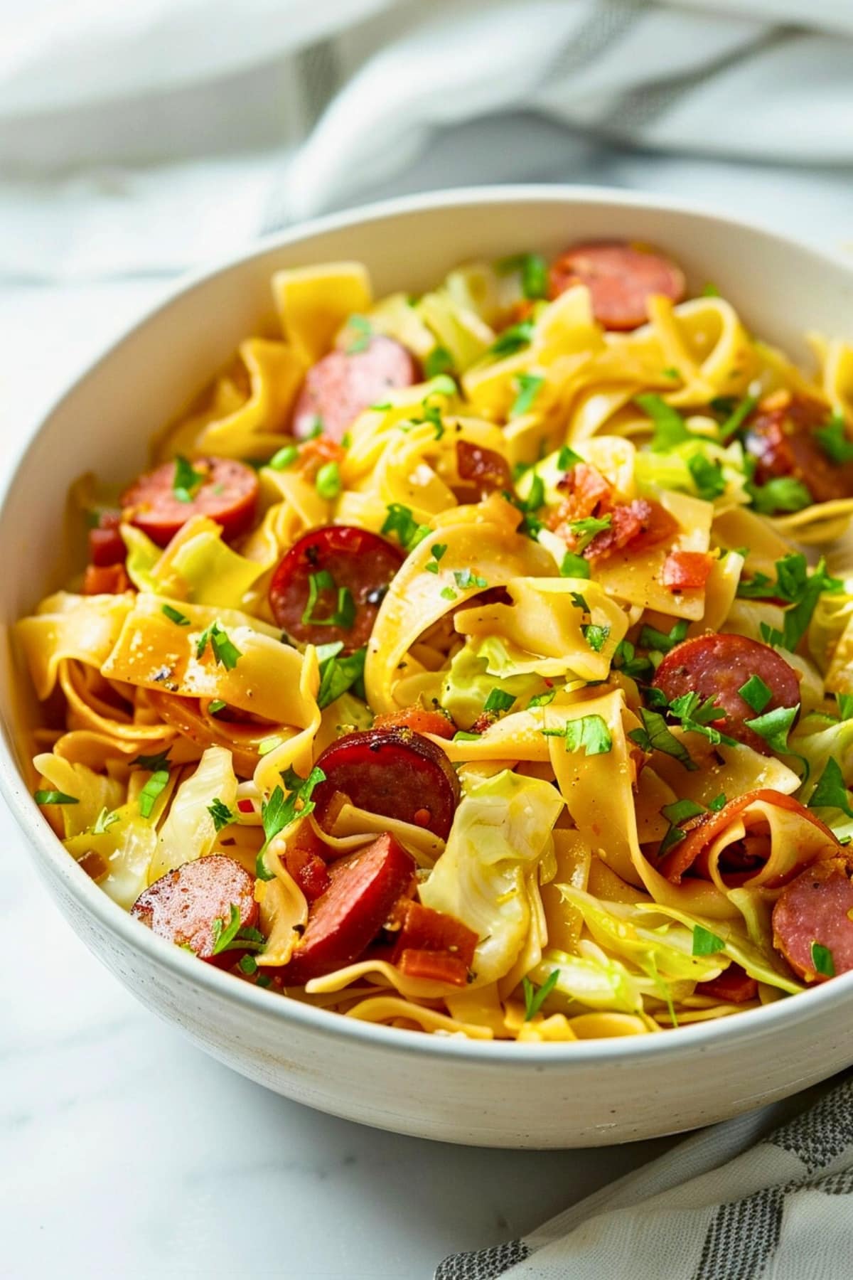 Buttery haluski with cabbage, kielbasa and egg noodles served on a white bowl.
