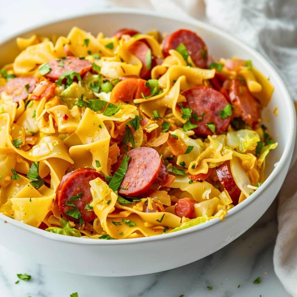 White bowl with servings of haluski, made with egg noodles, cabbage and kielbasa.