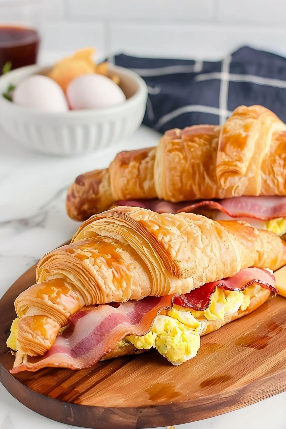 Breakfast croissant with crispy bacon and fluffy scrambled eggs in a wooden board