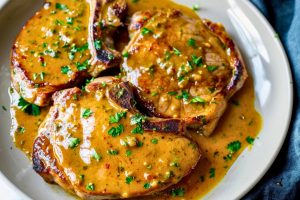 Pork chops served with honey mustard sauce on a plate garnished with chopped parsley.