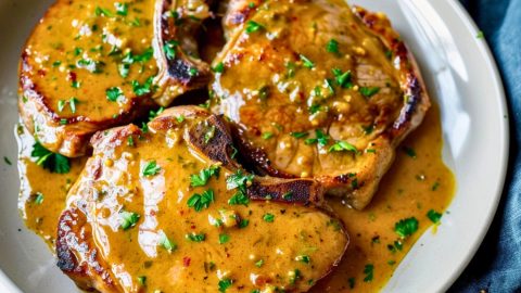 Pork chops served with honey mustard sauce on a plate garnished with chopped parsley.