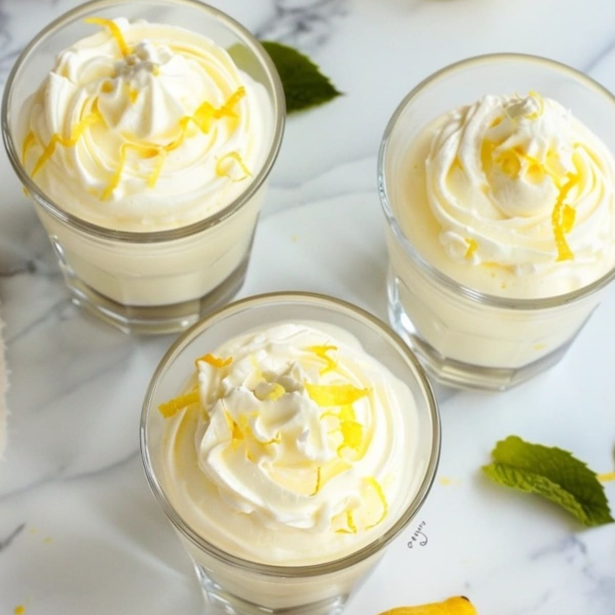 Lemon mousse served in glasses on a white marble table.
