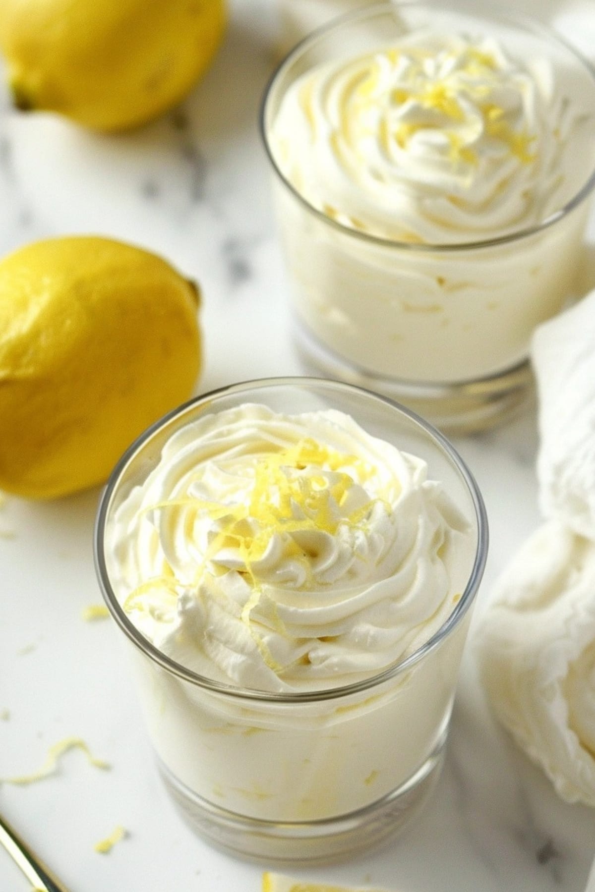 Lemon mousse on serving glasses garnished with lemon zest.