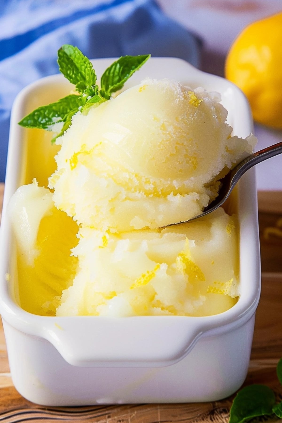 Lemon sorbet in a square dish scooped with a spoon, garnished with mint leaves.