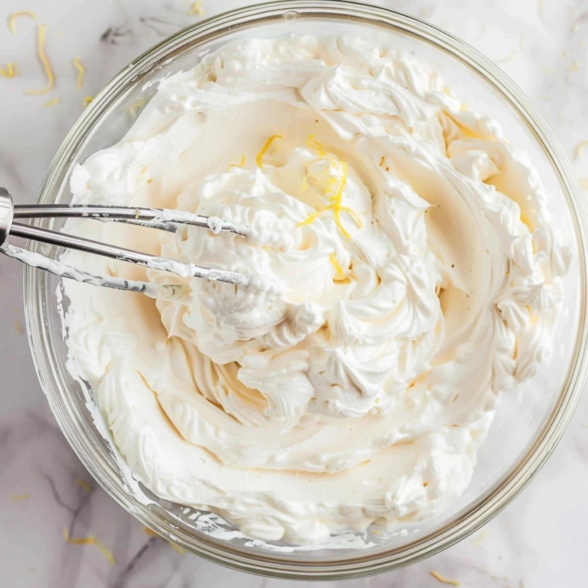 Whipped cream in a glass bowl with lemon zest.