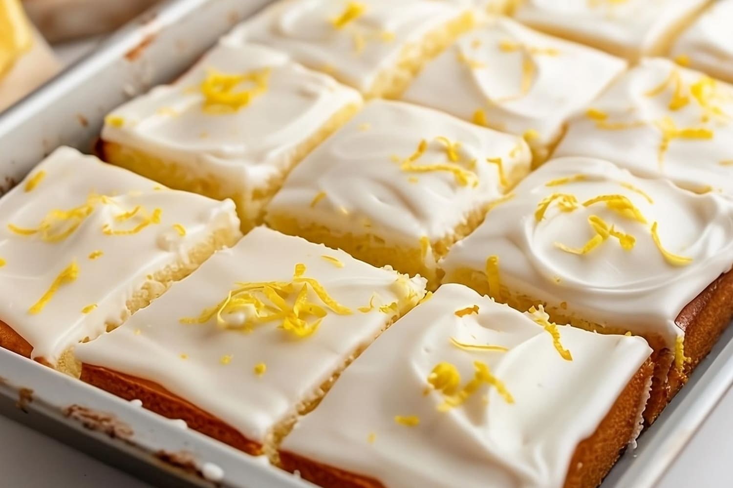 Sliced lemon sheet cake with sugar glaze and lemon zest garnish on top.