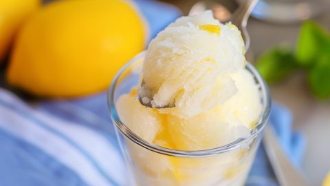 Spoon scooping lemon sorbet served on a glass.