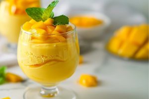 Mango mousse in a glass garnished with diced ripe mangoes and mint leaves.