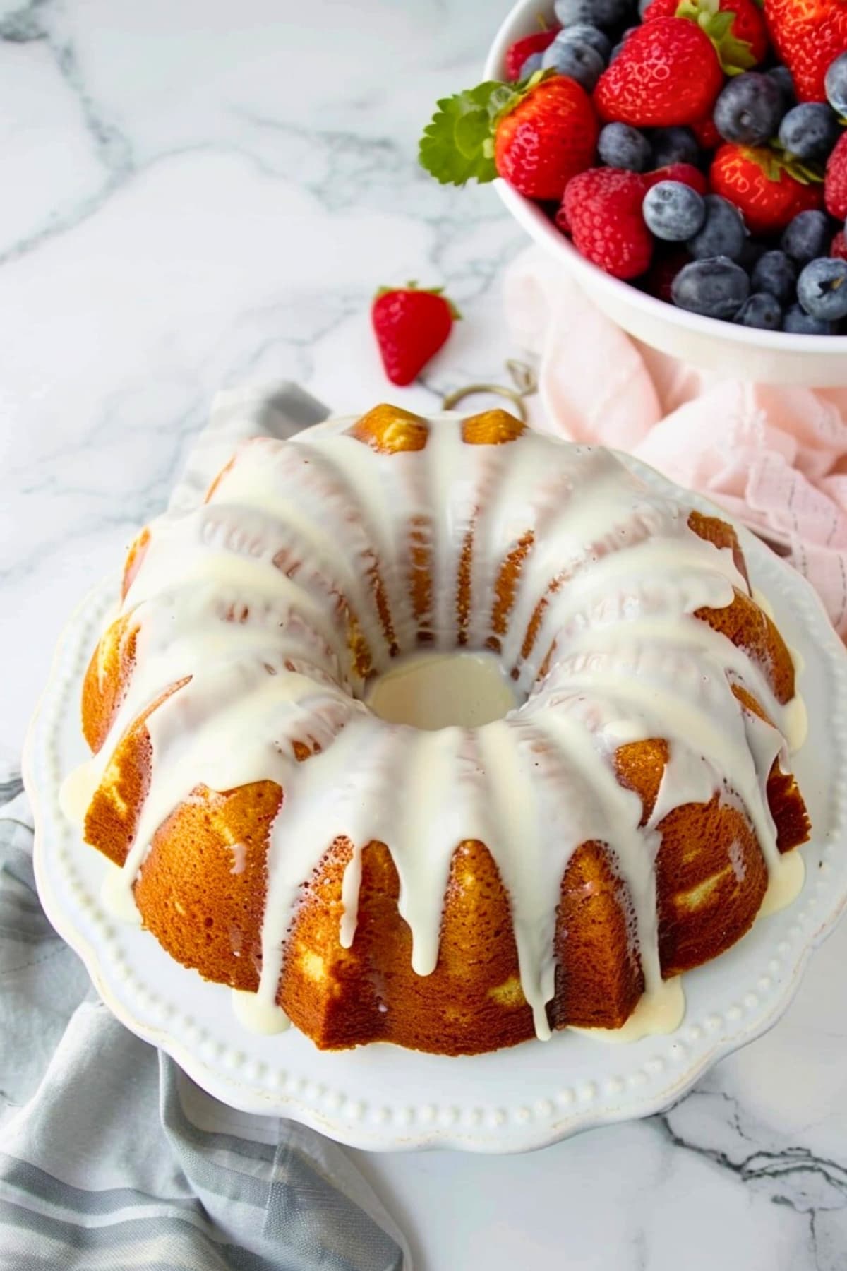 Million dollar pound cake with dripping sugar glaze on a cake tray, a bowl of berries on the side.