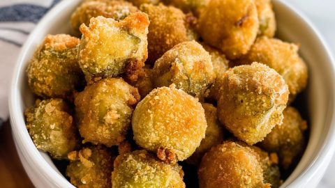 Bunch of coated fried okra in white bowl.