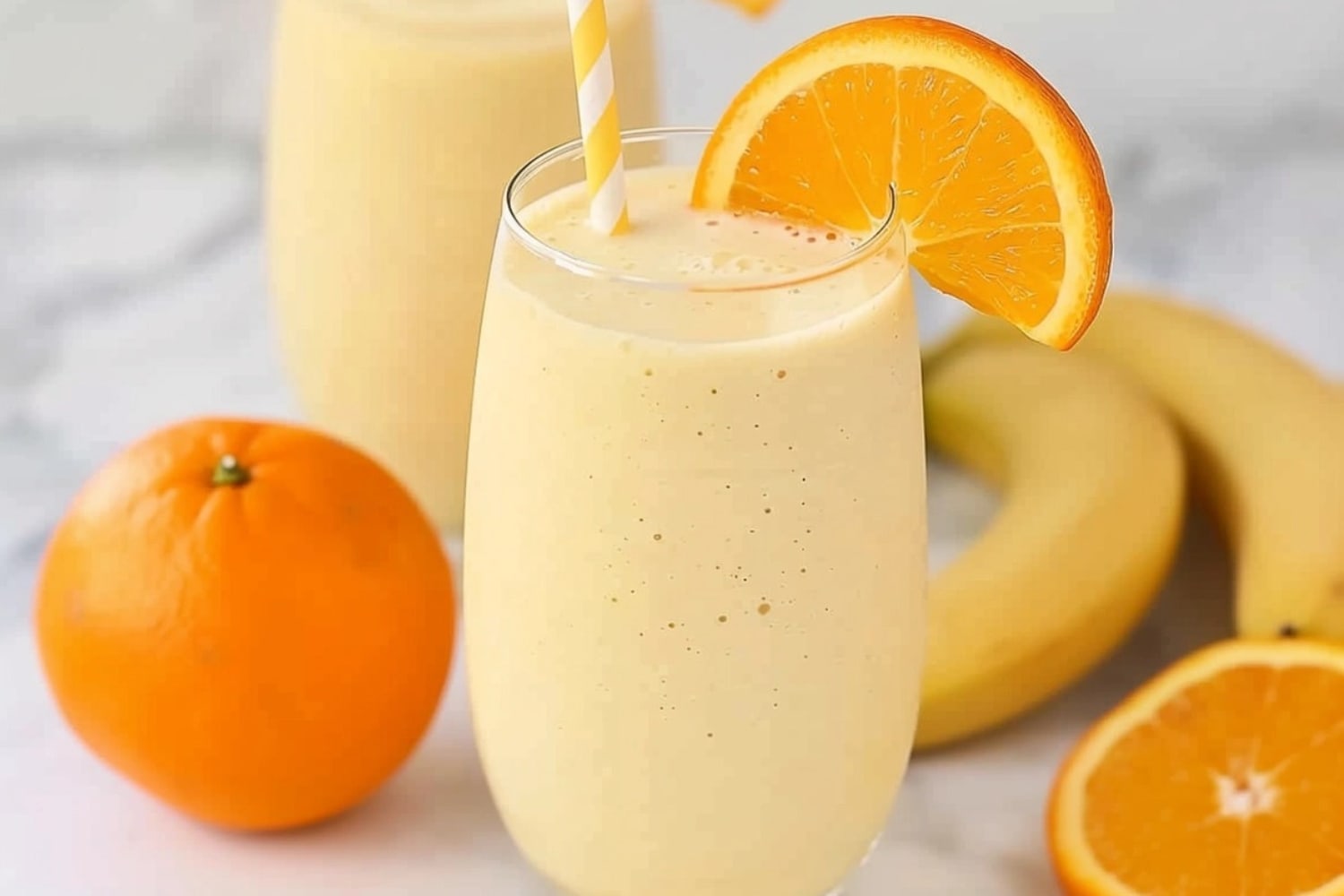 Glass of orange creamsicle smoothie with fresh bananas and orange beside.