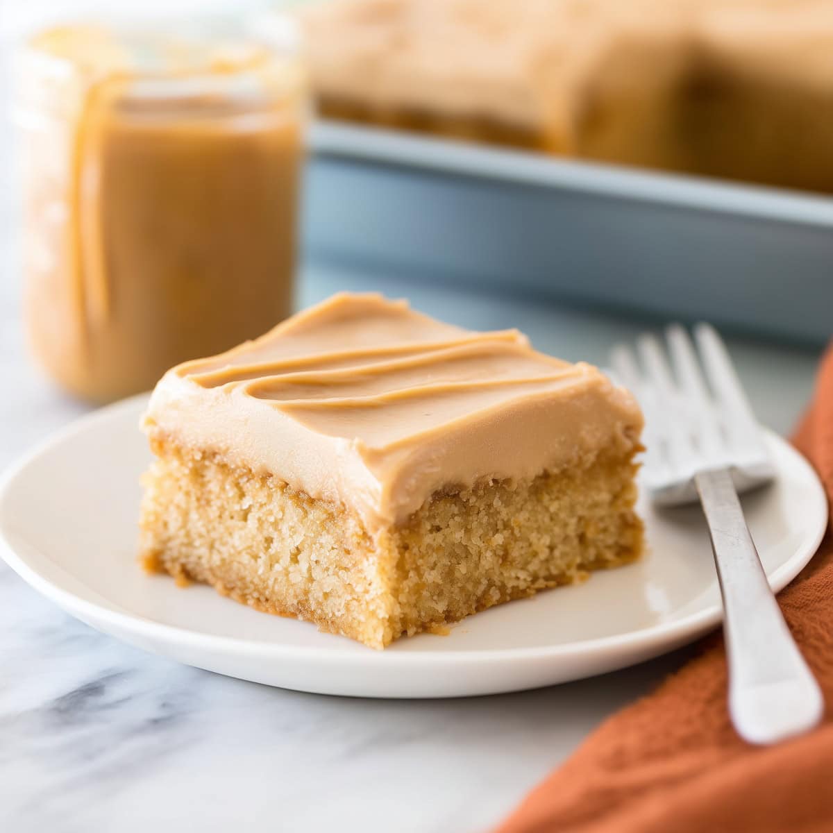 A square slice of peanut butter sheet cake in a plate with fork on the side.