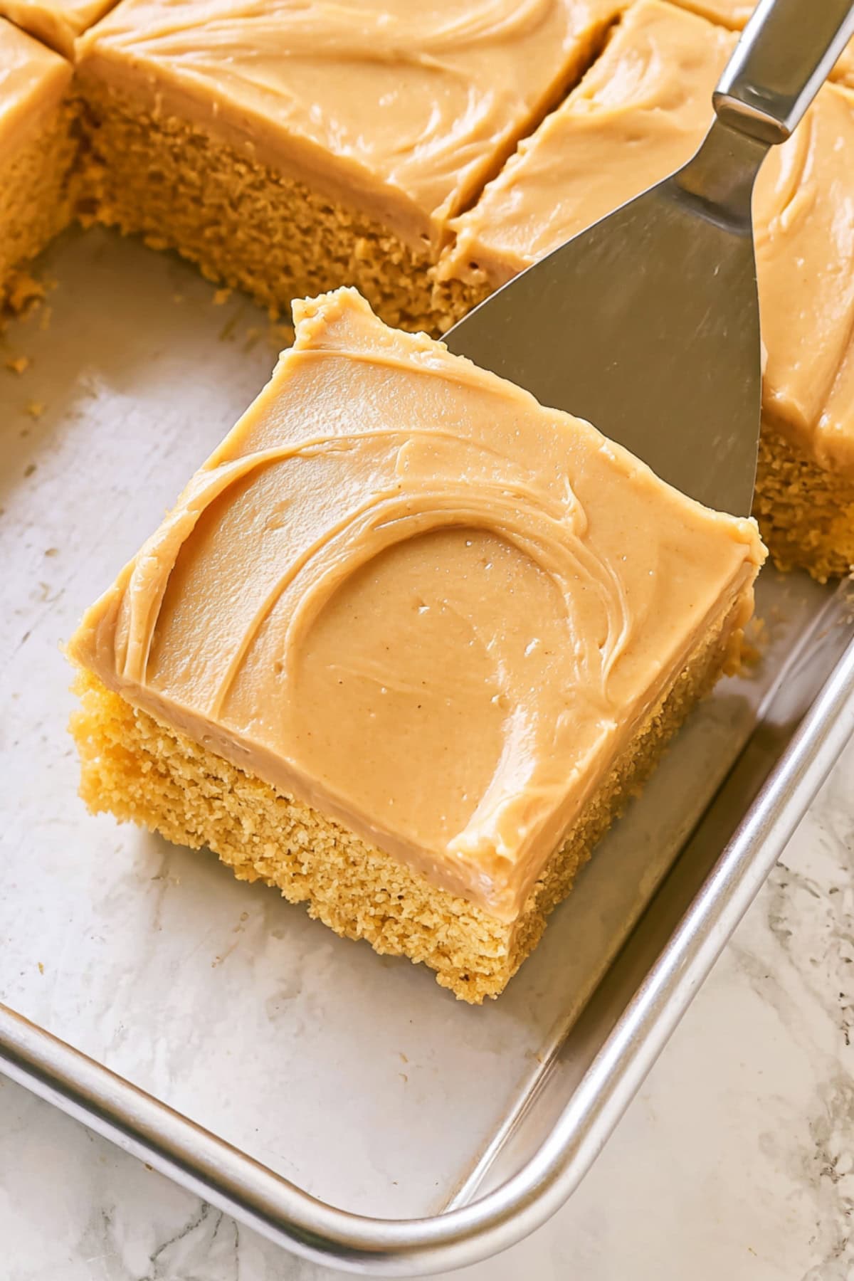 A close-up of peanut butter sheet cake with spatula in a sheet pan.