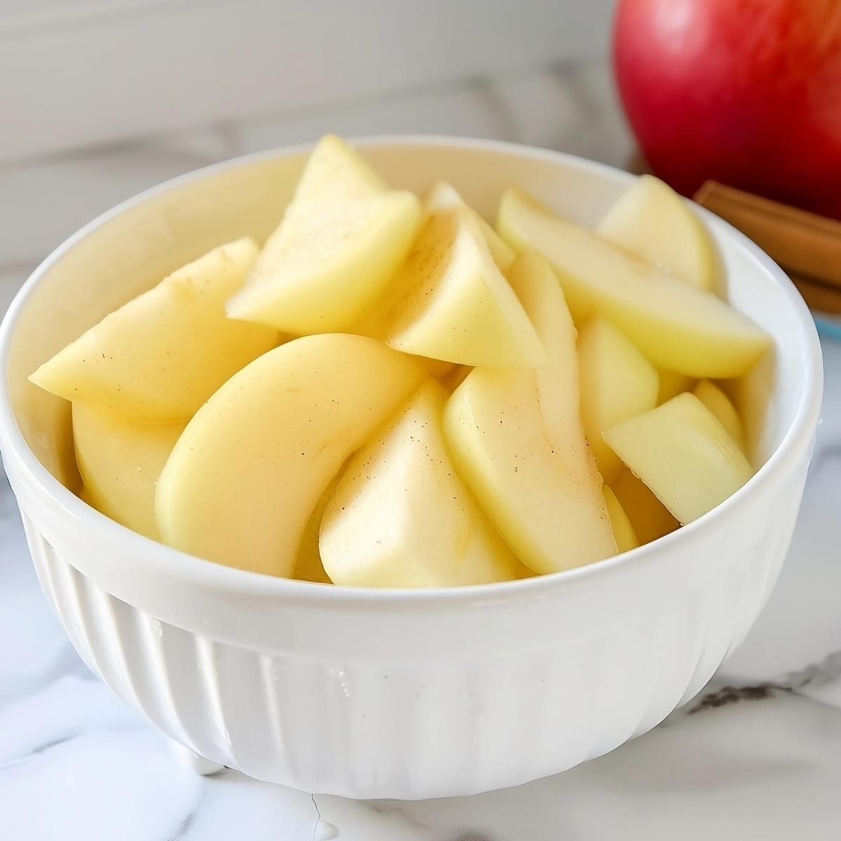 Peeled apple slices in white bowl.