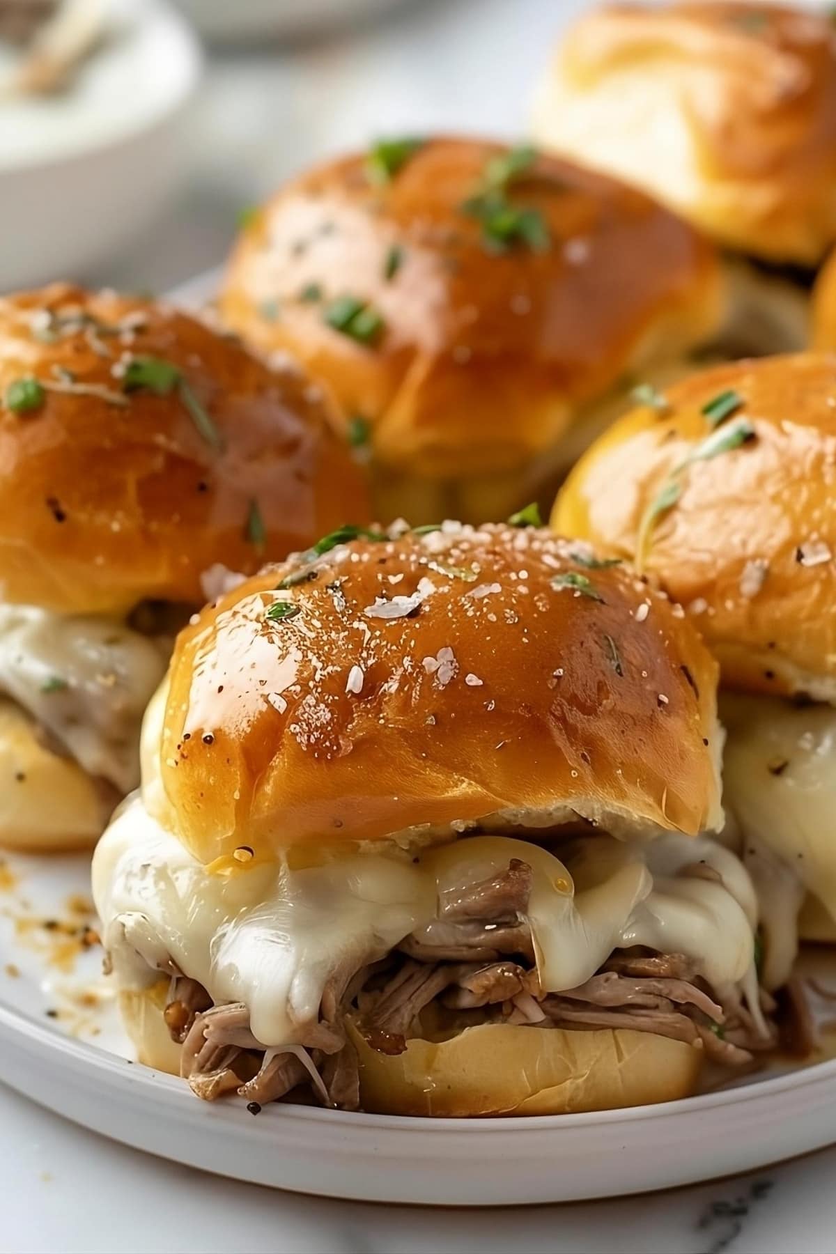 Philly Cheesesteak Sliders with melted cheese and shredded rib eye steak filling served on a white plate.