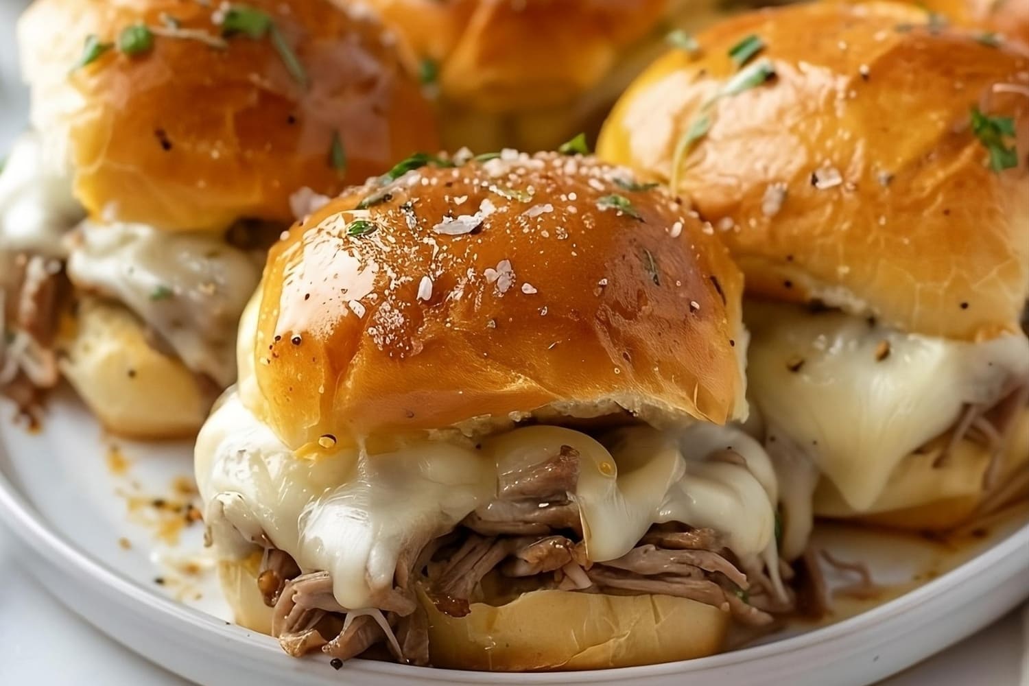 Philly Cheesesteak Sliders served on a white plate filled with melted cheese and beef filling.