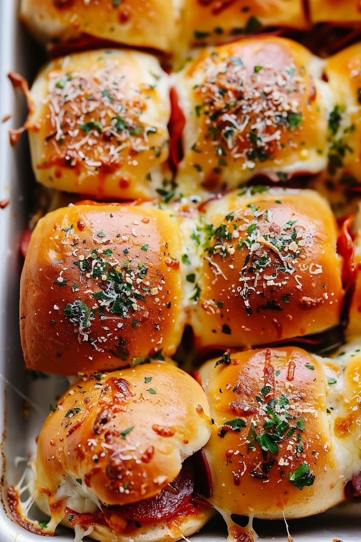 A pan filled with pizza sliders with herbs, pepperoni and tomato sauce