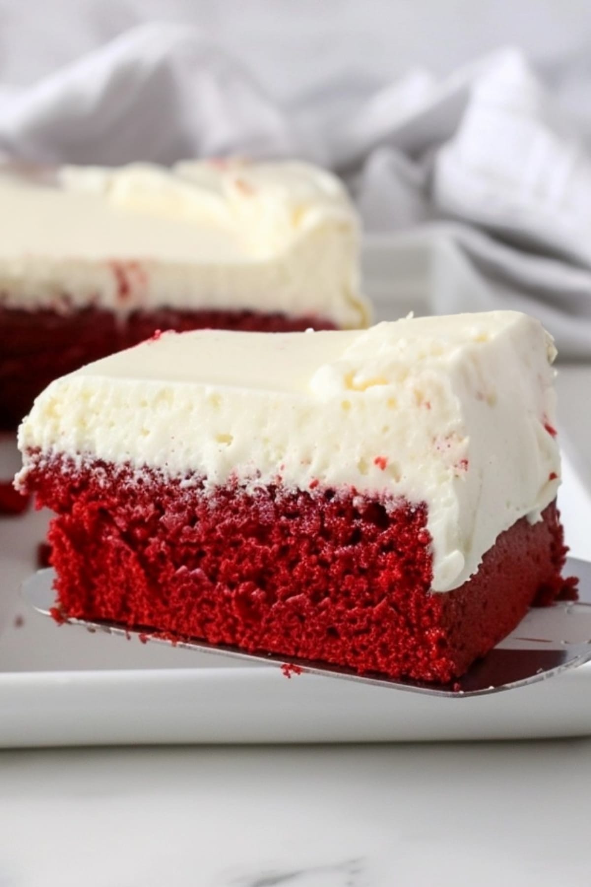 Cake ladle scooping a square slice of red velvet cake sheet.