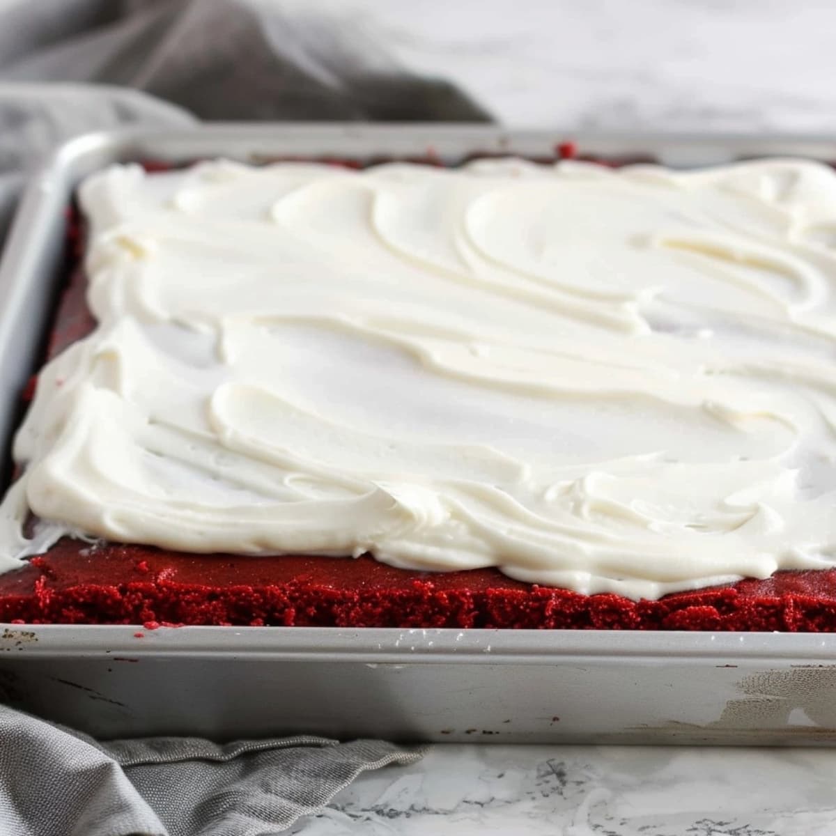 Red velvet sheet cake with spread of frosting on top.