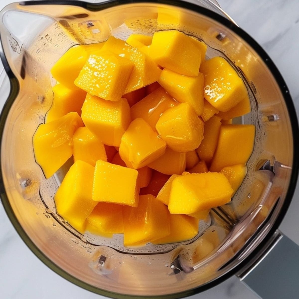 Cube cut ripe mangoes inside a blender pitcher with honey.