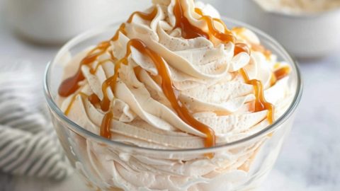 Salted caramel whipped cream drizzled with caramel syrup on a glass bowl.